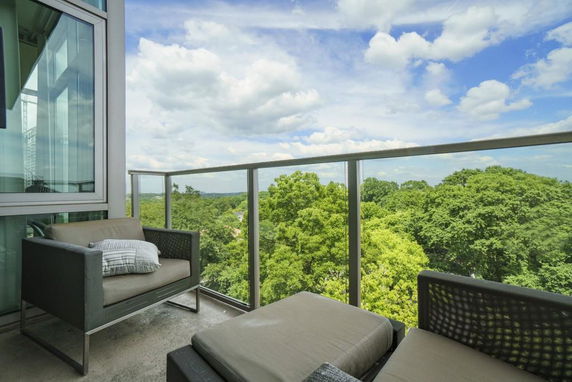 Balcony with outdoor seating and a view of trees and cloudy sky.
