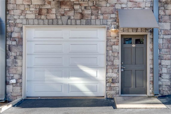 Front view of a garage door and a single door entrance with stone exterior.