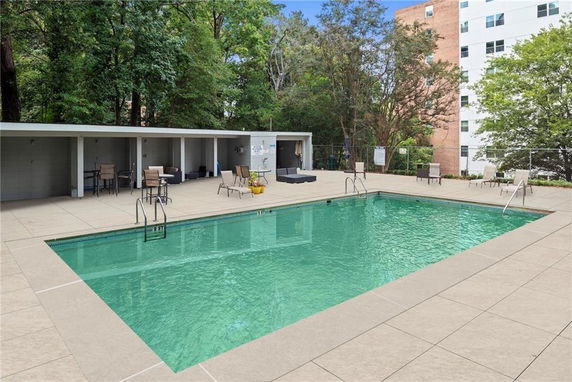 View of an outdoor swimming pool with surrounding seating and a building in the background.