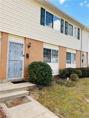 Front view of a two-story townhouse with a brick and siding exterior, featuring multiple windows and a metal door.