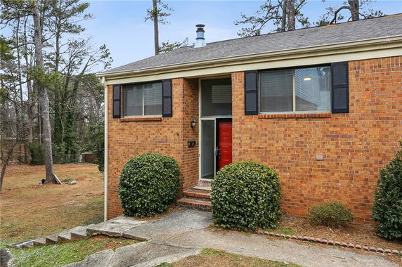 Front view of a brick house with a red door and two large windows.