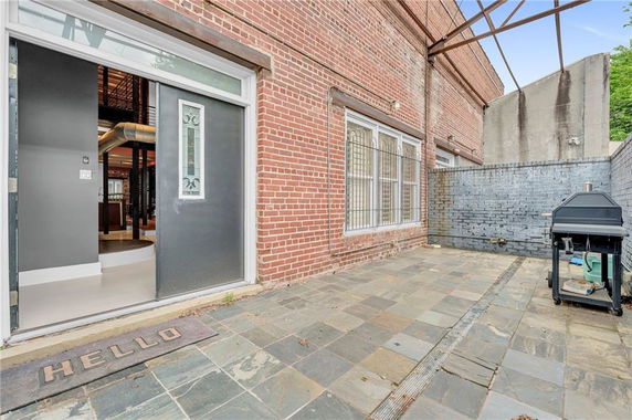 Outdoor view of a brick building with a patio and a barbecue grill.