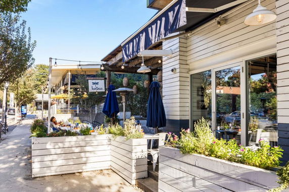 Front view of a restaurant with outdoor seating and blue umbrellas.