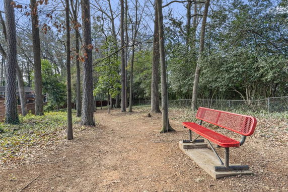 Pathway in a wooded area with a red metal bench and trees.