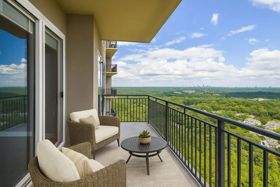 Balcony view with outdoor seating overlooking a vast green landscape and distant city skyline.