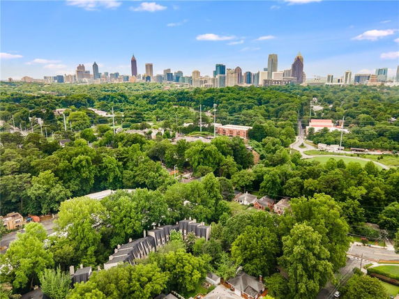 Wide-angle view of city skyline with buildings in the distance and lush green trees in the foreground.