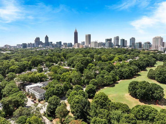 Panoramic view of a city skyline with numerous tall buildings and a large expanse of trees and parkland in the foreground.