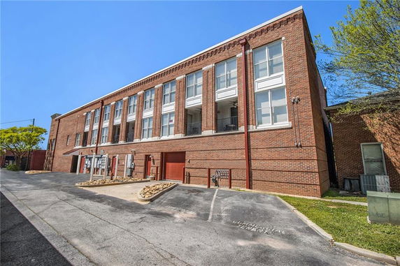 Front view of a multi-story brick building with large windows and a parking area.