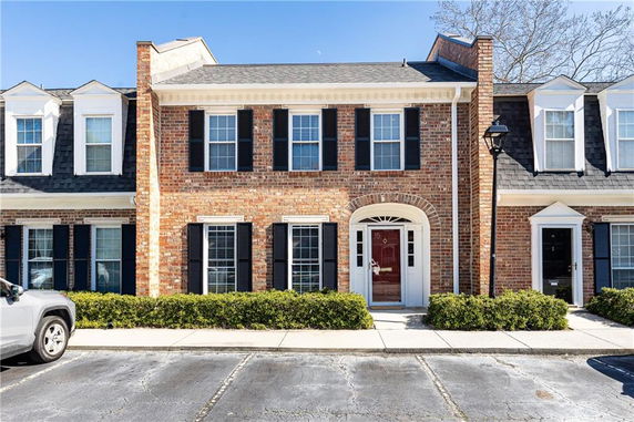 Front view of a two-story brick townhouse with black shutters and a red door.
