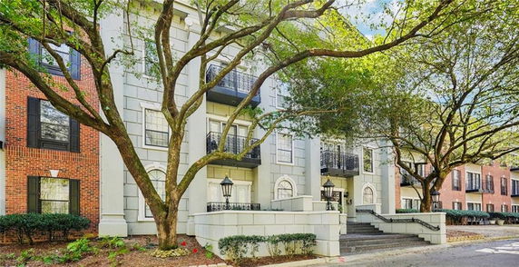 Front view of a multi-story residential building with brick and stone facade, featuring balconies and large trees.