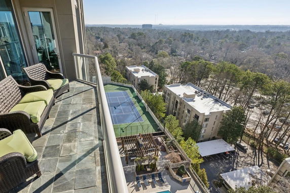 Balcony view showing tennis court and surrounding buildings with trees in the distance.