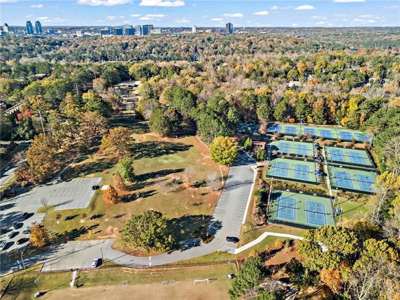 Aerial view of multiple tennis courts surrounded by trees and adjacent to a parking area.