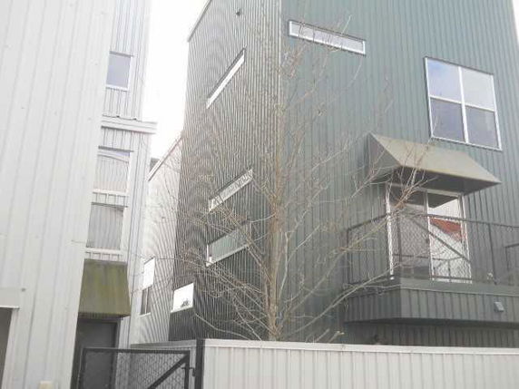 Front view of a tall building with corrugated metal siding and multiple windows.