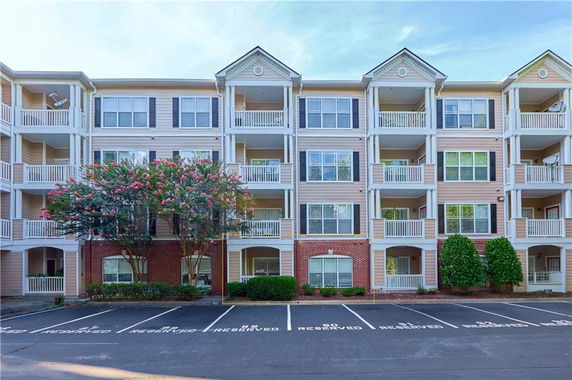 Front view of a multi-story apartment building with balconies and parking spaces.