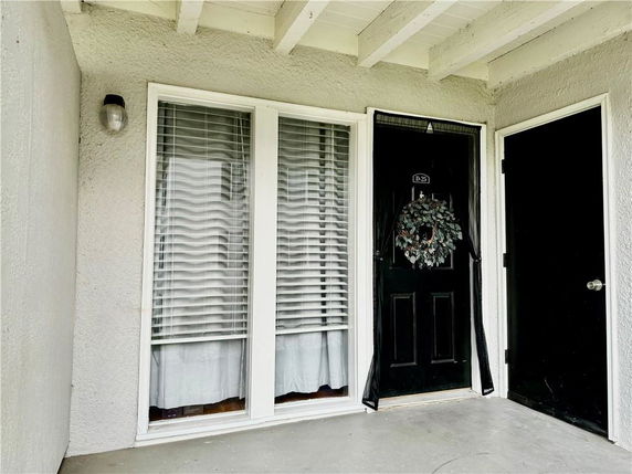 Front view of a home entrance with a black door and adjacent windows with blinds.