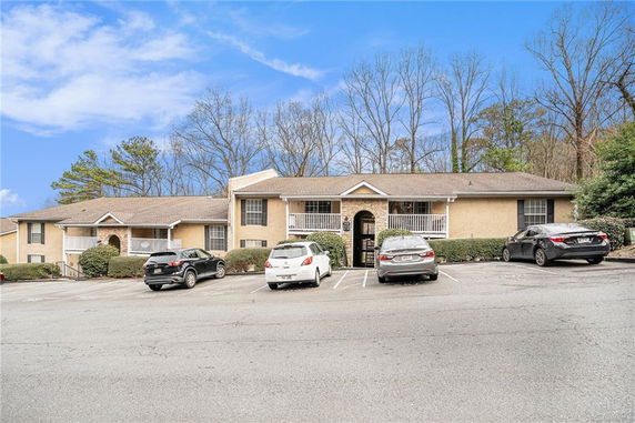 Front view of a residential building with a parking area and surrounding trees.