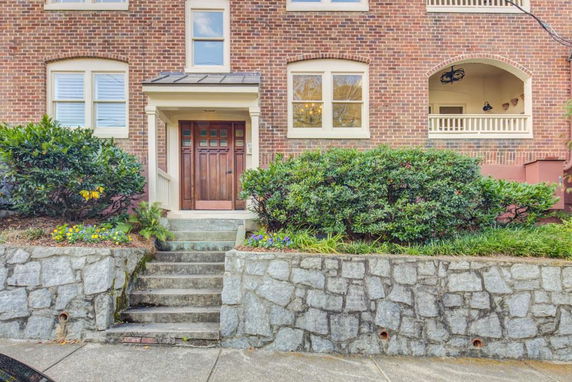 Front view of a brick residential building with a porch and stone steps leading to the entrance.