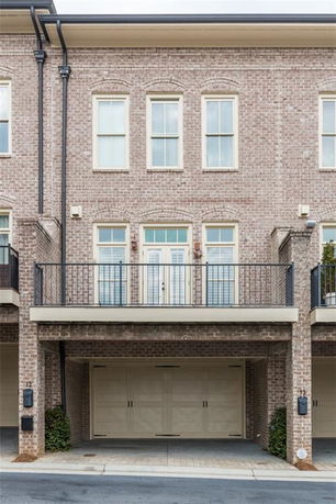 Front view of a multi-story brick townhouse with a small balcony and a double garage.