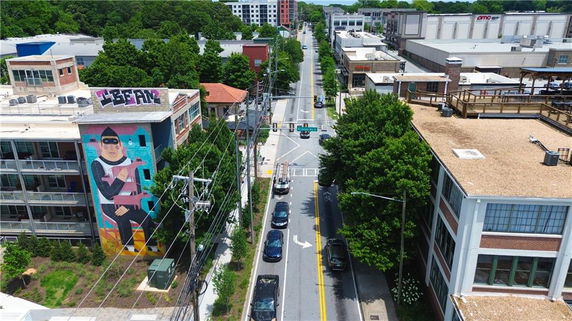 Aerial view of a street lined with buildings, graffiti on one building, and trees along the sidewalk.
