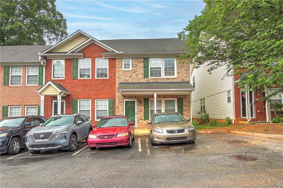 Front view of a two-story townhouse with a brick facade and adjacent parking area.