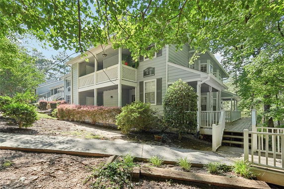 Front view of a two-story house with a porch and balcony, surrounded by greenery.
