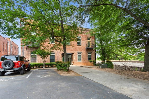Front view of a brick two-story building with surrounding trees and nearby parking.