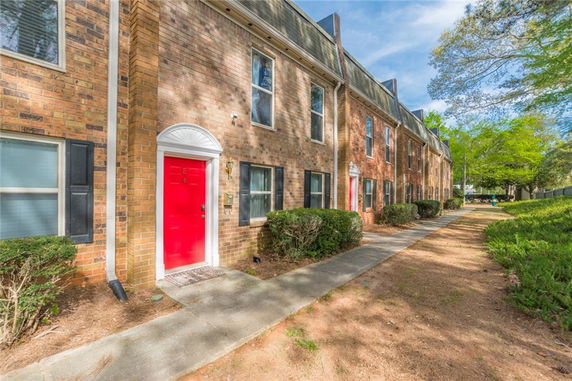 Front view of a multi-story brick townhouse with red doors and a sidewalk.