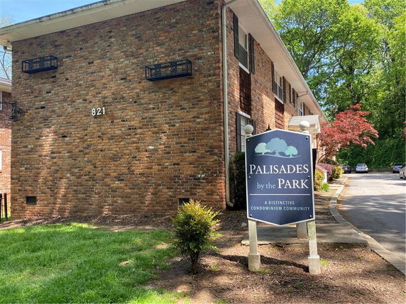 Front view of a brick condominium building with a sign and parking area.