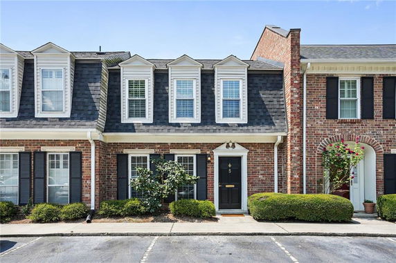 Front view of a two-story brick townhouse with dormer windows and a black front door.