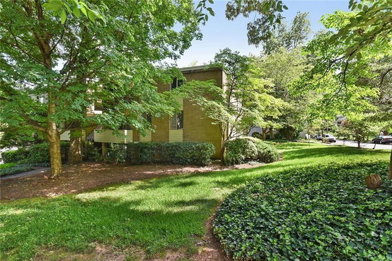 Front view of a two-story house surrounded by lush greenery and trees.