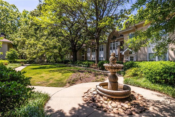 View of a landscaped area with a fountain and a multi-story residential building in the background.