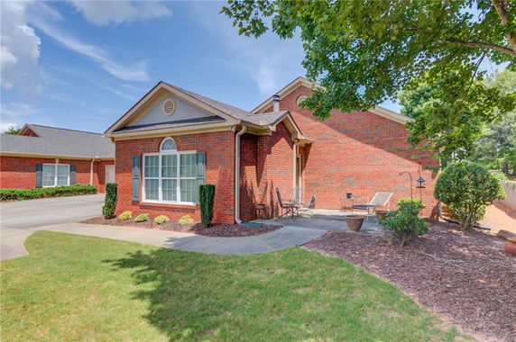 Front view of a single-story brick house with a curved driveway and small outdoor sitting area.
