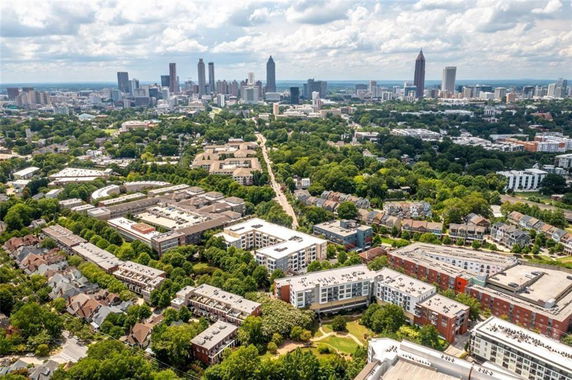 Aerial panoramic view of a cityscape with multiple residential and commercial buildings, surrounded by greenery and a distant skyline.