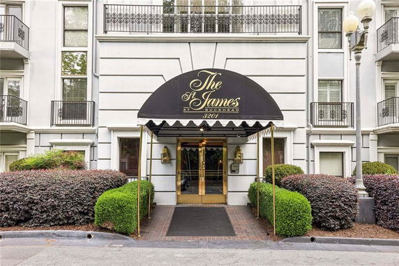 Front view of a building entrance with a black awning and surrounding landscaping.