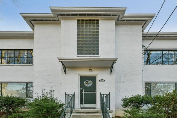 Front view of a white brick two-story building with a central glass block window and green door.