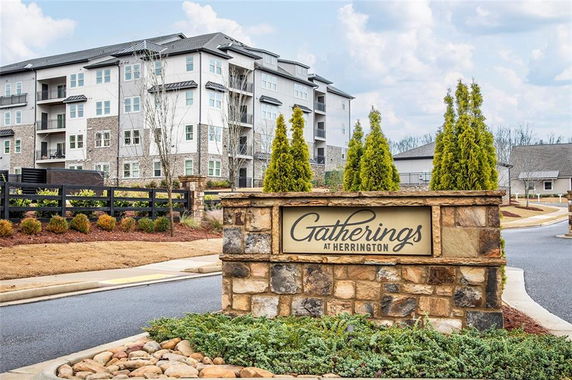 Front view of a multi-story apartment building with a stone sign in the foreground.