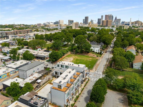 Aerial view of a cityscape with residential and commercial buildings, trees, and skyscrapers in the distance.