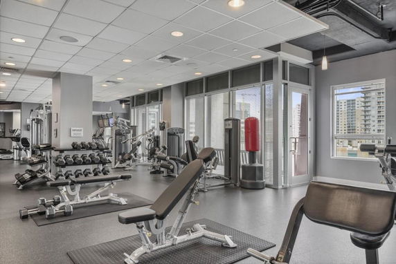 Indoor gym area with various exercise equipment and a window view of buildings.