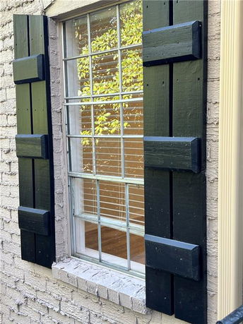 View of a single window with black shutters on a brick wall.