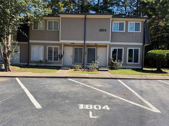 Front view of a two-story residential building with a light and dark color scheme, featuring multiple windows and a parking area in front.