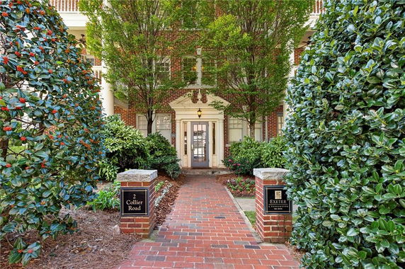 Front view of a brick building entrance with decorative pillars and greenery.