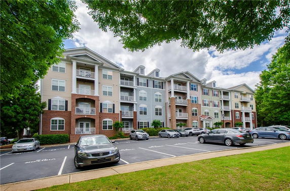 Front view of a multi-story apartment building with balconies and parking spaces.