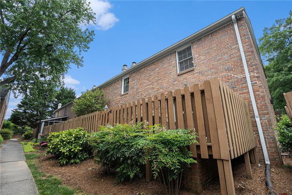 Side view of a brick house with a wooden fence and a walkway.
