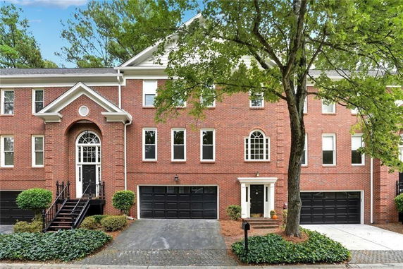 Front view of a brick multi-story house with three black garage doors and a central entrance.