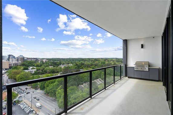 A spacious balcony with a glass railing overlooking a cityscape and greenery.