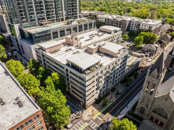 Aerial view of a multi-story building complex with adjacent structures and lush green surroundings.