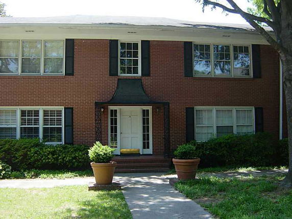 Front view of a two-story brick house with large windows and a central entrance.