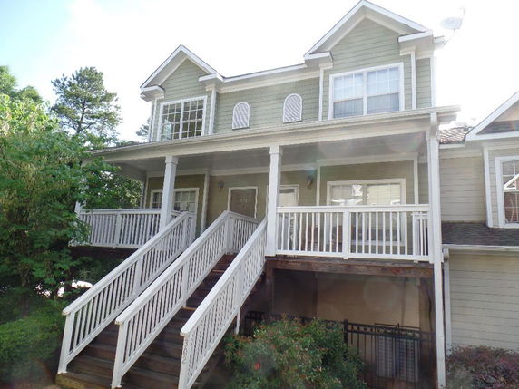 Front view of a two-story house with a porch and twin staircases leading to the entrance.