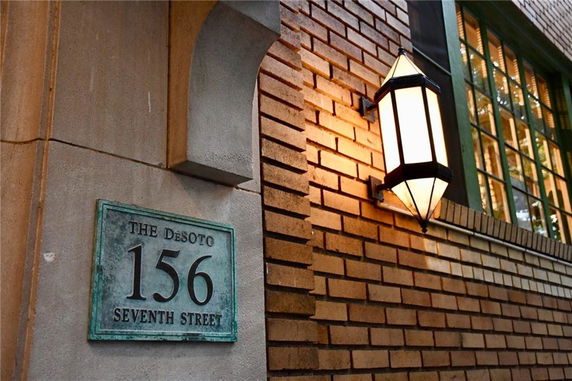 Building exterior with bricks, a wall-mounted light, and a nameplate with the address.