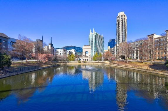 Cityscape view with modern buildings and a pond with a fountain in the foreground.